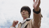 a man in a brown jacket is standing in front of a cloudy sky with his arms outstretched .