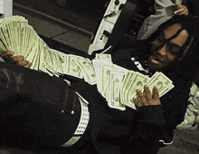 a man is laying on the ground holding a stack of 20 dollars