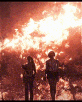 two people are standing in front of a fire