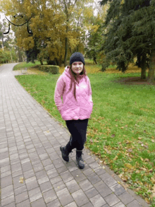 a girl in a pink jacket and black hat is walking down a path
