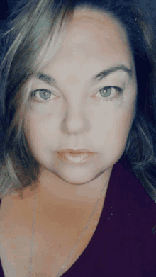a close up of a woman 's face with a purple shirt on