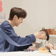 a man feeding a baby with korean writing on the bottom of the picture