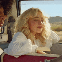 a woman with blonde hair is sitting in the back seat of a car looking out the window