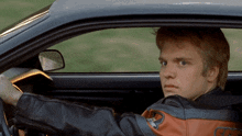 a man wearing a harley davidson jacket is driving a black car