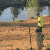 a man in a yellow shirt is standing in front of a body of water .