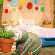 a stuffed animal in a room with a potted plant and a bed in the background