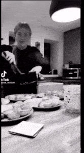a black and white photo of a woman cooking in a kitchen with plates of food on the counter