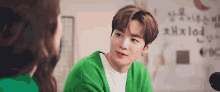a man in a green sweater is talking to a woman in a white shirt .