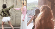 a group of girls are standing next to each other in front of a wall . one of the girls is wearing headphones .