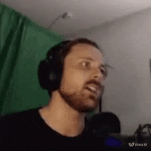 a man with a beard is wearing headphones and making a funny face in front of a green screen .