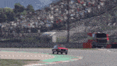 a red car is driving down a race track with a crowd in the background