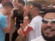 a man wearing sunglasses is standing in a crowd of people holding a red cup .