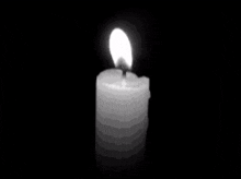 a black and white photo of a lit candle on a black background .