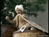 a man in a turban is sitting on top of a barrel holding a snake .