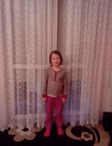 a little girl stands in front of a white curtain
