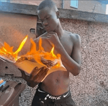 a shirtless man wearing nike shorts is holding a burning book