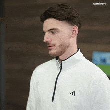 a man wearing a white adidas jacket stands in front of a sign that says canirove