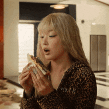 a woman in a leopard print jacket is eating a sandwich .