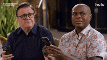 two men looking at their phones with a hulu logo in the corner