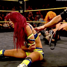 a woman with red hair is laying on the ground in a wrestling ring being held by a man .