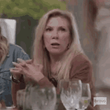 a woman is sitting at a table with wine glasses and clapping her hands .