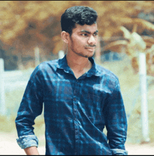 a young man wearing a blue plaid shirt is standing in front of a fence