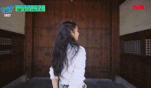 a woman with long black hair is standing in front of a wooden door in a building .