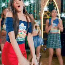 a woman wearing a blue shirt that says our stories christmas is dancing in front of a group of girls .