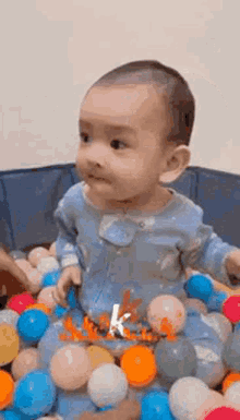 a baby is sitting in a ball pit filled with balls and looking at the camera .