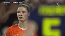 a female soccer player stands in front of a scoreboard that says 5 on it