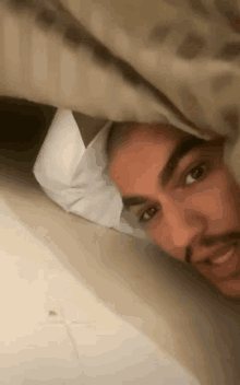 a man with a beard is laying on a bed under a blanket .