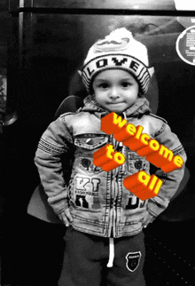 a little boy wearing a hat that says love is standing in front of a sign that says welcome to all