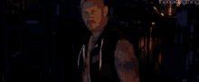 a man is standing in a dark room wearing a black vest that says wwe