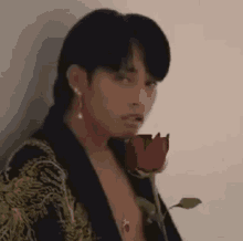a man is holding a red rose in his hand and looking at the camera .