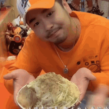 a man in an orange shirt holds a bowl of food in his hands