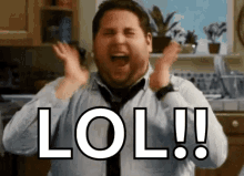 a man in a tie is laughing in a kitchen with his hands in the air and the word lol written on his face .
