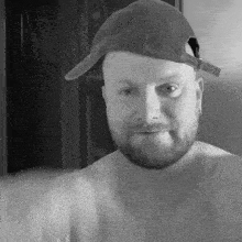 a man with a beard is wearing a baseball cap without a shirt .