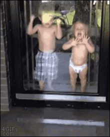 two babies in diapers are standing in front of a glass door