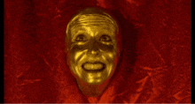 a gold face with a red background is smiling and looking at the camera