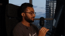 a man wearing glasses and ear buds is sitting in front of a microphone in front of a window