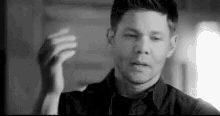 a black and white photo of a man in a black shirt holding his hand up .