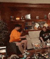 a man in an orange shirt is sitting on a couch playing a guitar