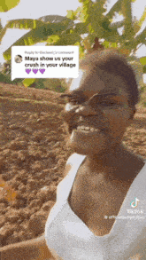 a woman in a white tank top is smiling in front of a field of dirt .