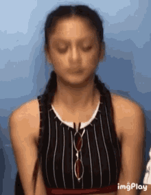 a woman wearing a striped tank top and sunglasses is making a funny face with her eyes closed .