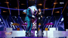 a man in a suit stands on a stage in front of a mask singer logo