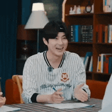 a young man is sitting at a table with a pen in his hand and laughing .
