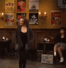 a woman is dancing in a bar with posters on the wall .