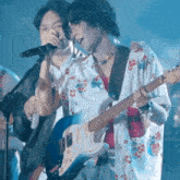 a man singing into a microphone while another man plays guitar