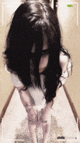 a woman with long black hair is standing in a hallway with a cell phone behind her