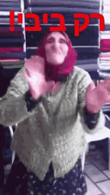 a woman in a green sweater and a red head scarf is dancing in front of a pile of fabric